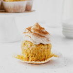 healthier carrot cake cupcakes with liner peeled off on with more cupcakes on a cakestand in the background.