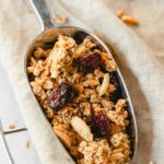 christmas spiced granola with cranberries on vintage serving spoon on beige background.