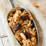 christmas spiced granola with cranberries on vintage serving spoon on beige background.