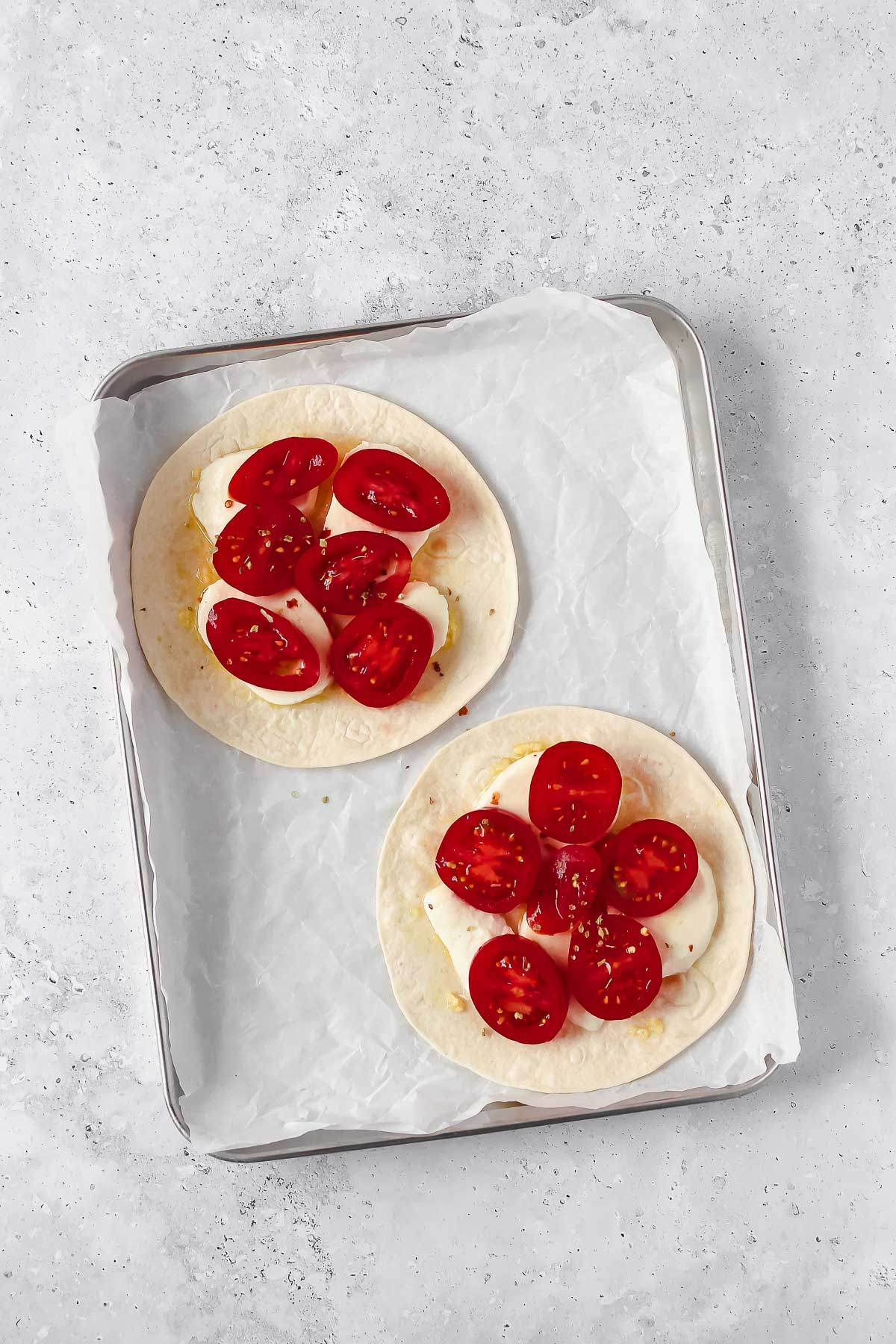 preparing tortilla pizza on baking sheet with olive oil, garlic, mozzarella and tomatoes