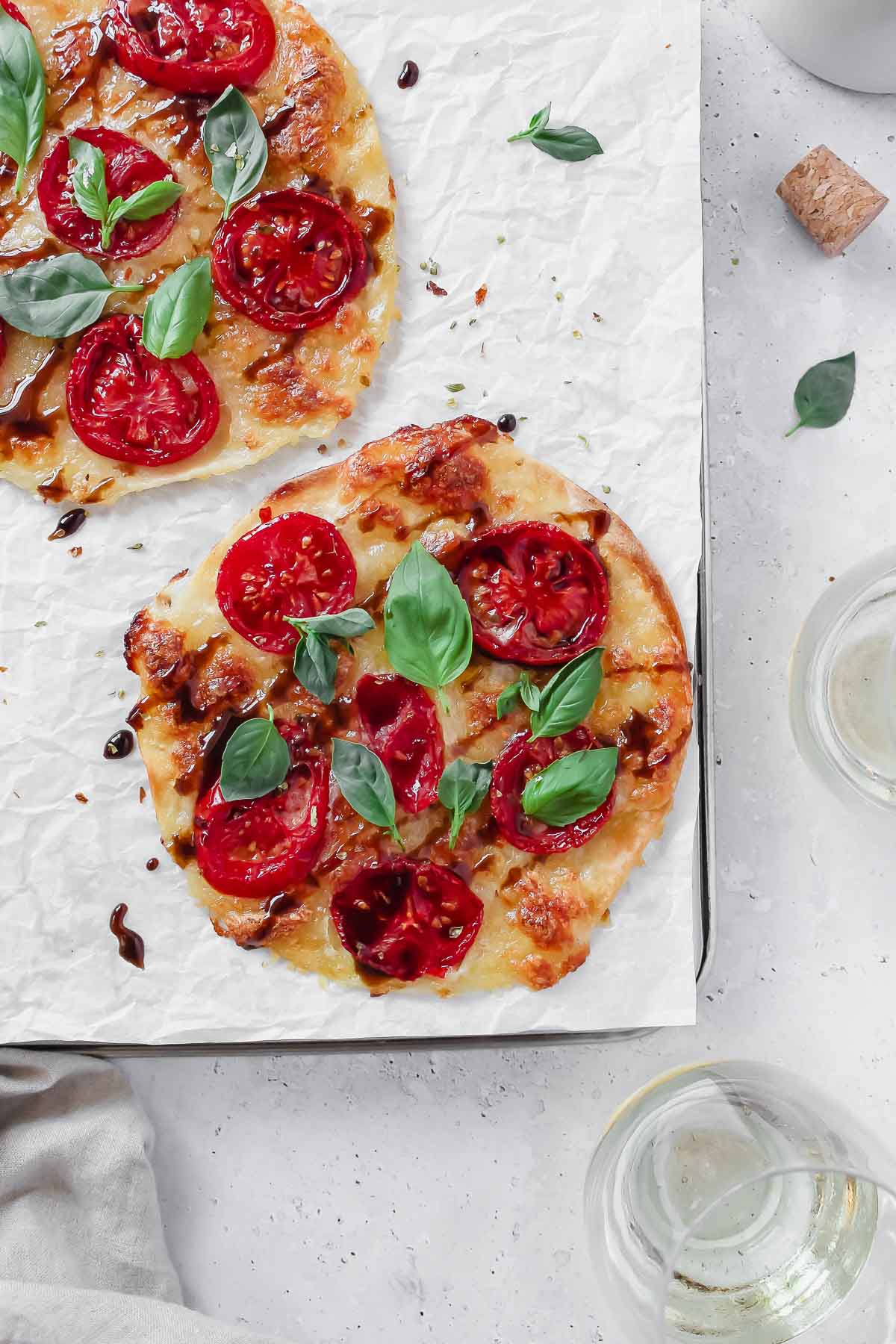 caprese tortilla pizza on baking sheet with parchment paper on grey background with wine glass and linen