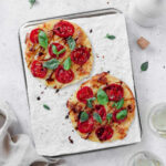 caprese tortilla pizza on baking sheet with parchment paper on grey background with wine glass and linen