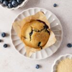 blueberry buttermilk muffin in brown cupcake liner on dusty rose background with blueberries and brown sugar decoration