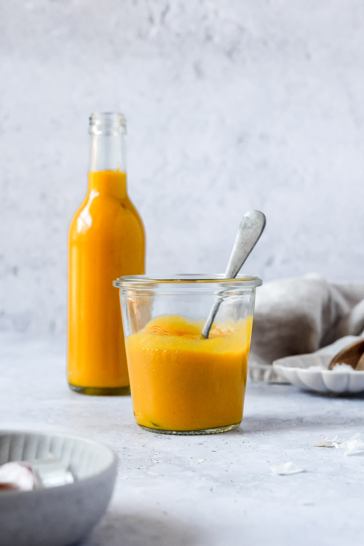 spicy mango sauce in weck jar and bottle standing on grey blue background with vintage spoon