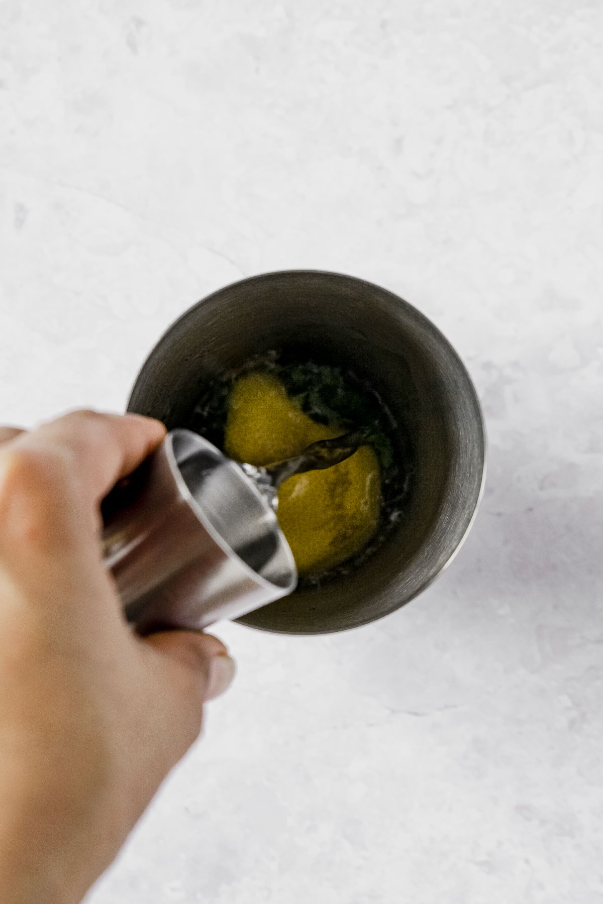 pouring gin into cocktail shaker with lemon, basil and agave syrup.