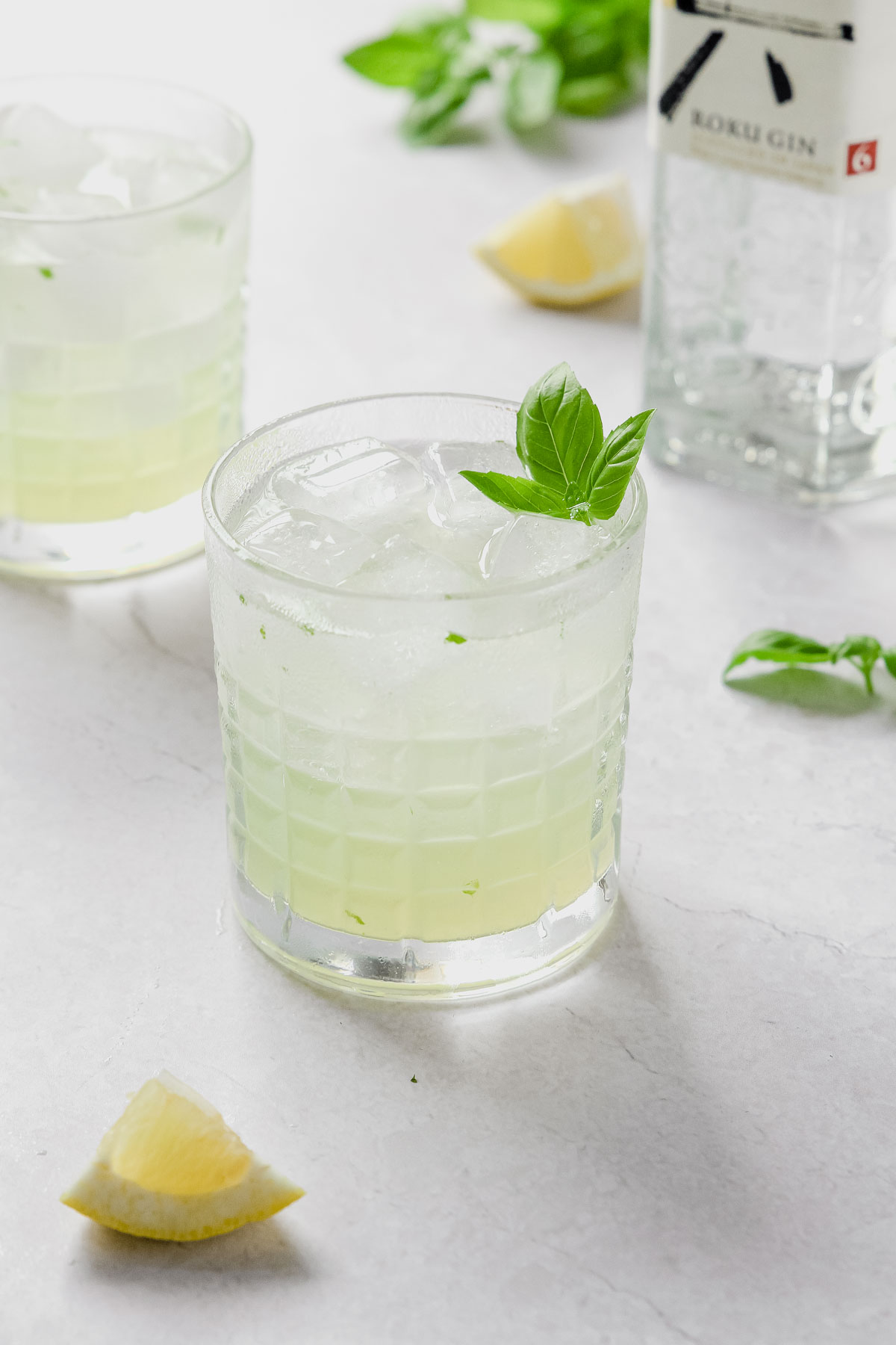 gin basil smash with lemon and roku gin on grey marble background.