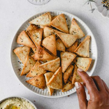 reaching for baked pita chips with everything bagel seasoning on grey plate with hummus