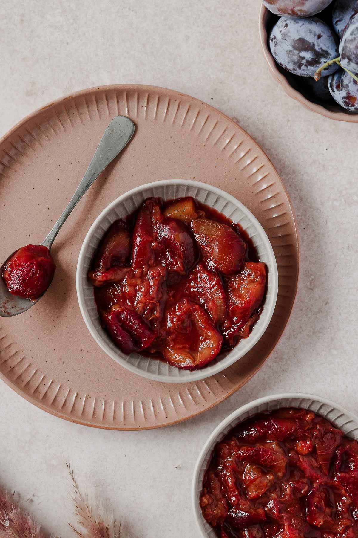 plum compote in grey bowl with vintage spoon on dusty rose plate