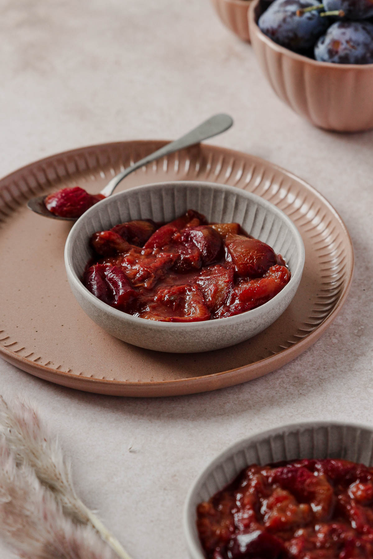 plum compote in grey bowl with vintage spoon on dusty rose plate