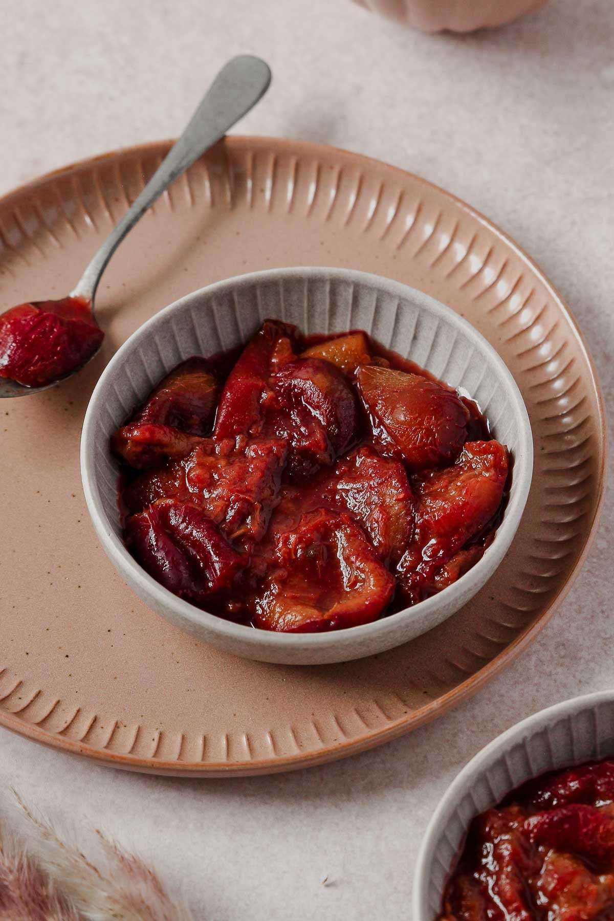 plum compote in grey bowl with vintage spoon on dusty rose plate