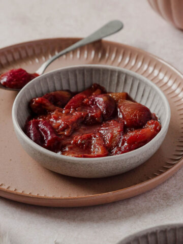 plum compote in grey bowl with vintage spoon on dusty rose plate