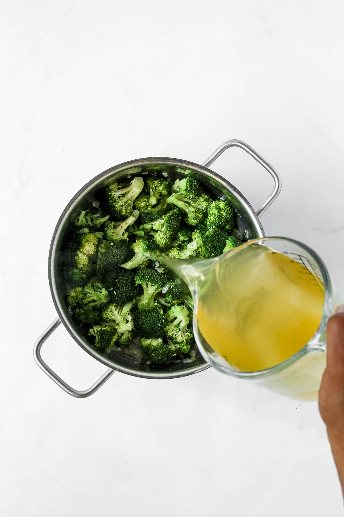 pouring vegetable stock into pot of roasted broccoli, onion and garlic.