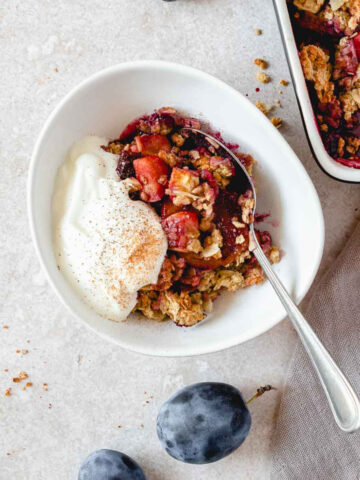 apple and plum crumble in bowl with yoghurt with vintage spoon