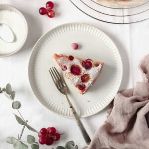 piece of grape cake on white plate with vintage fork with grapes, linen and yoghurt on white background.