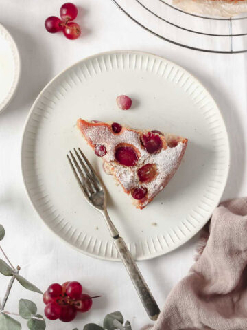 piece of grape cake on white plate with vintage fork with grapes, linen and yoghurt on white background.