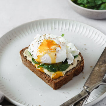 healthy breakfast bread with spinach, hummus and poached egg on grey plate with vintage cutlery.