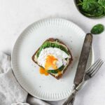 healthy breakfast bread with spinach, hummus and poached egg on grey plate with vintage cutlery.