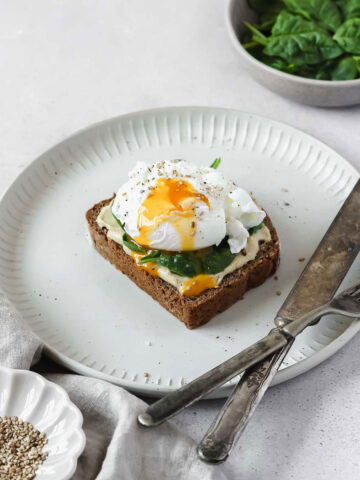 healthy breakfast bread with spinach, hummus and poached egg on grey plate with vintage cutlery.