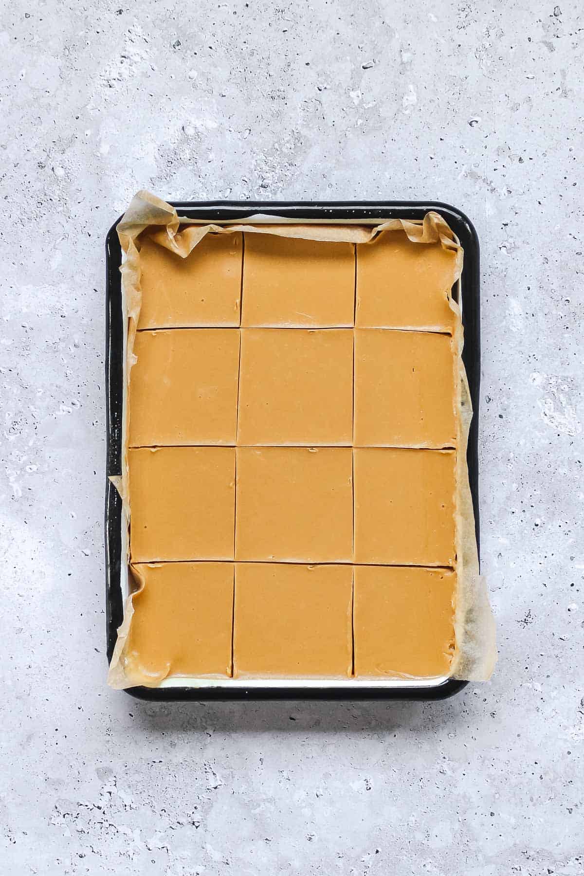 peanut butter fudge cut into squares in baking pan on blue background.