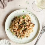 bacon and mushroom pasta on off white plates with vintage fork on beige rose background with props.