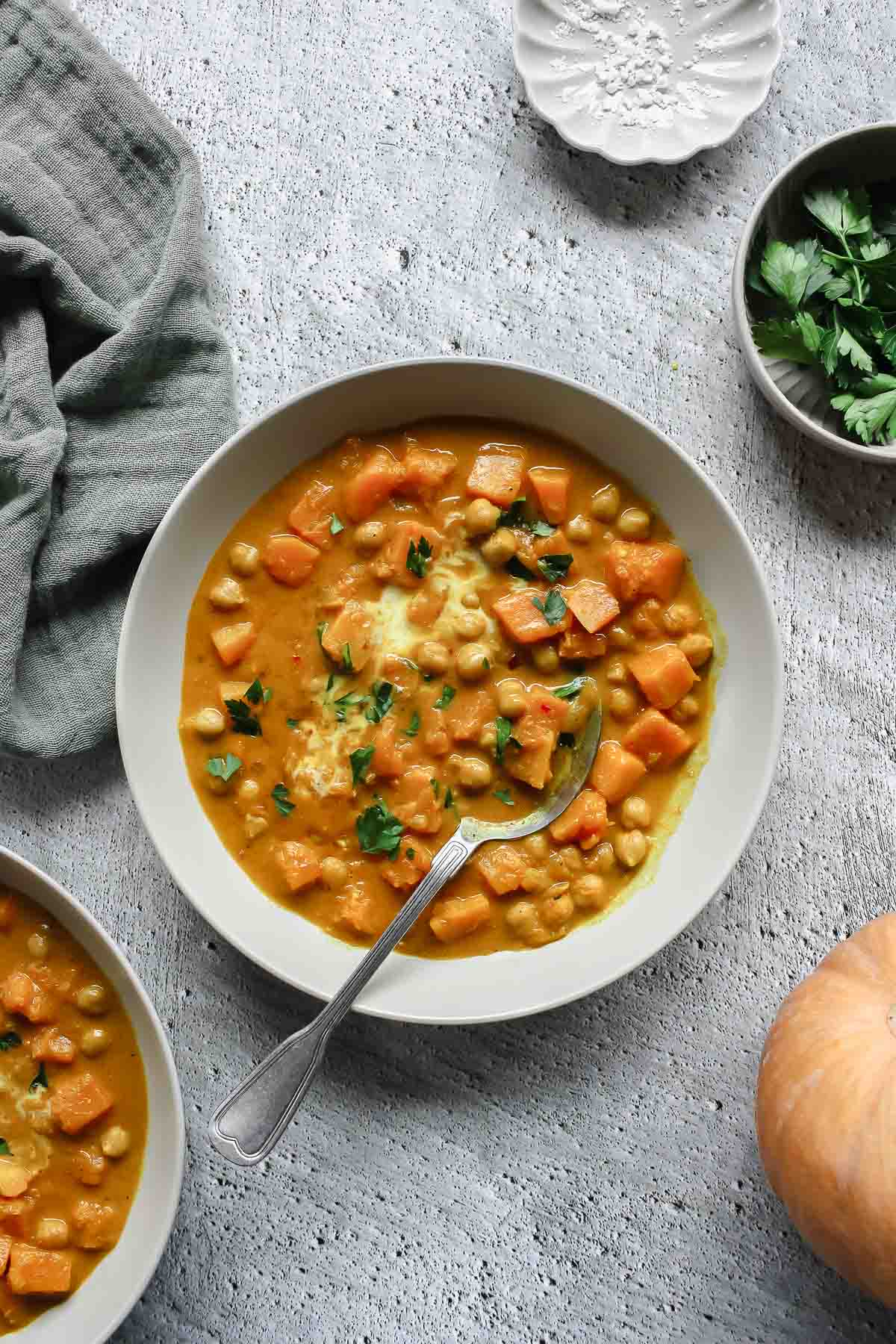 butternut squash curry in soup bowl with vintage spoon on grey backdrop with props.