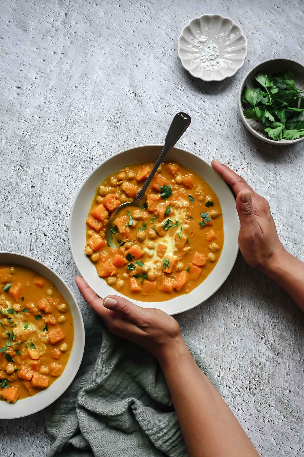 butternut squash curry in soup bowl with vintage spoon on grey backdrop with props.