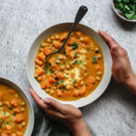 butternut squash curry in soup bowl with vintage spoon on grey backdrop with props.