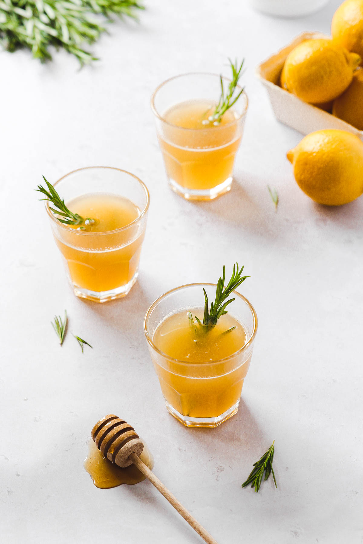 lemon drops with honey and rosemary garnish on light grey background with props.