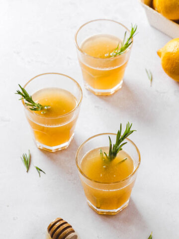 lemon drops with honey and rosemary garnish on light grey background with props.