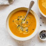 pumpkin soup in beige bowl with vintage spoon on beige background.