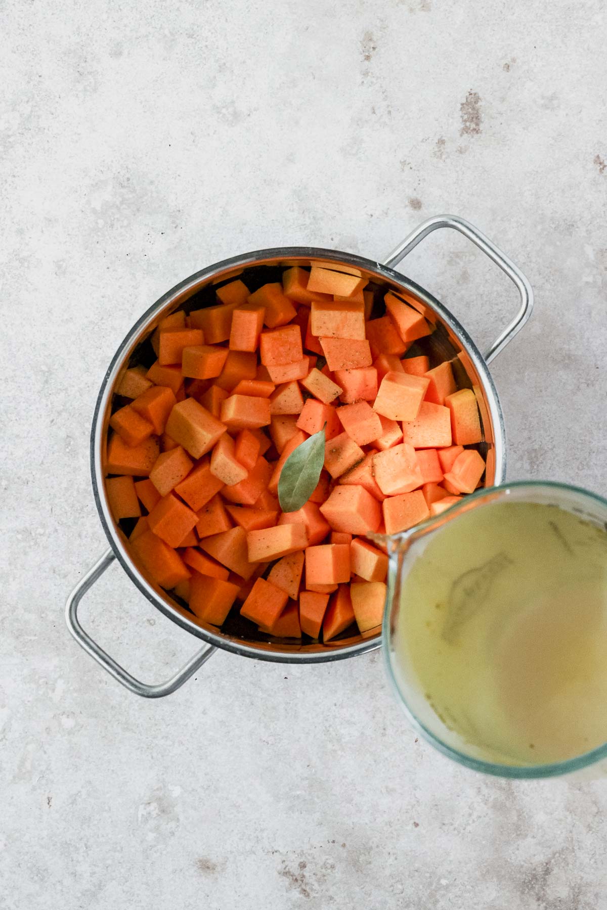 pouring vegetable stock into roasted pumpkin and spices in pot.