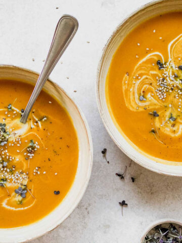 pumpkin soup in beige bowl with vintage spoon on beige background.