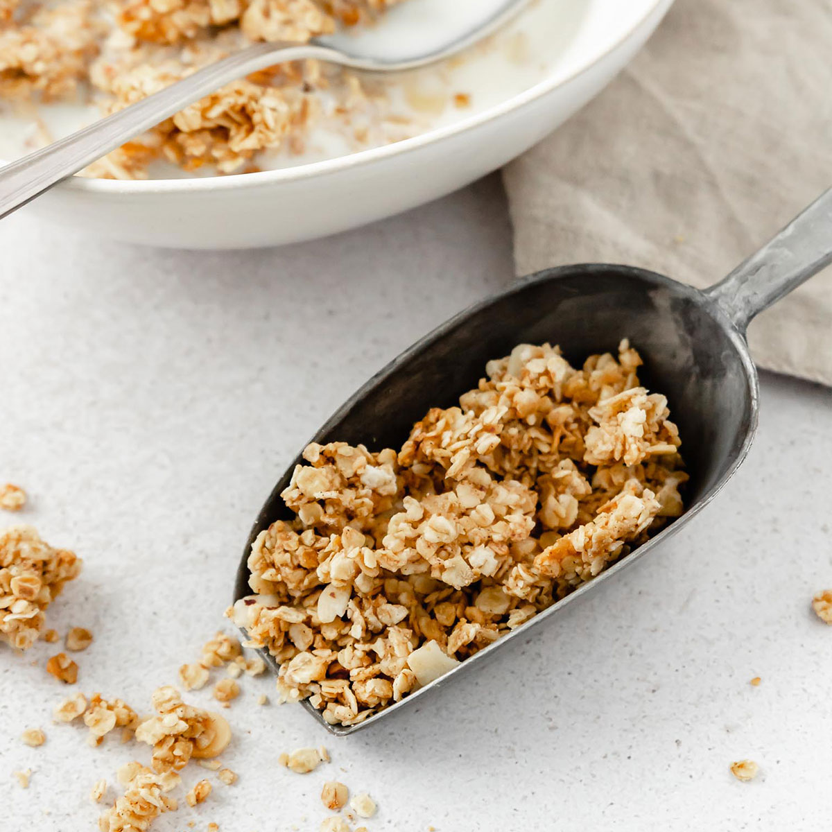 almond granola in serving shovel with granola and milk bowl in the background.