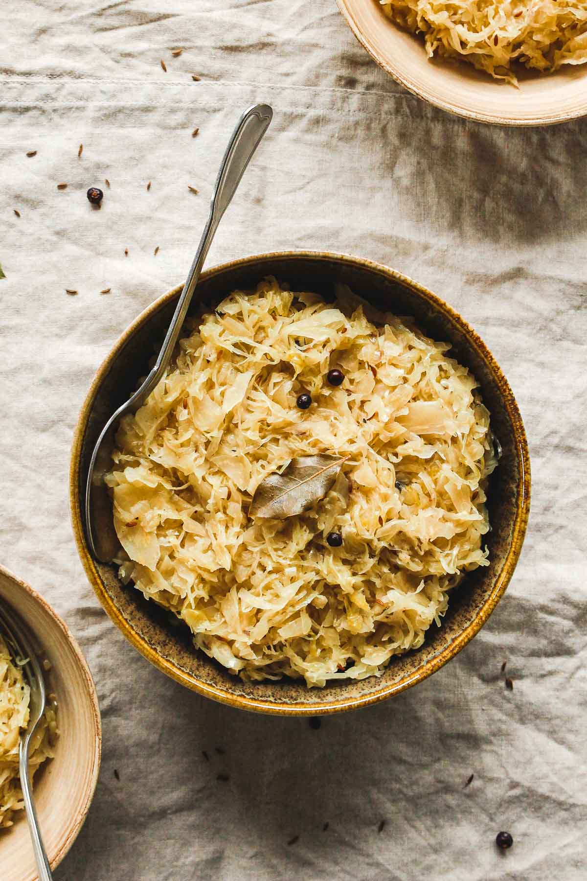 aromatic cooked sauerkraut in brown bowls with vintage spoon on beige tablecloth.