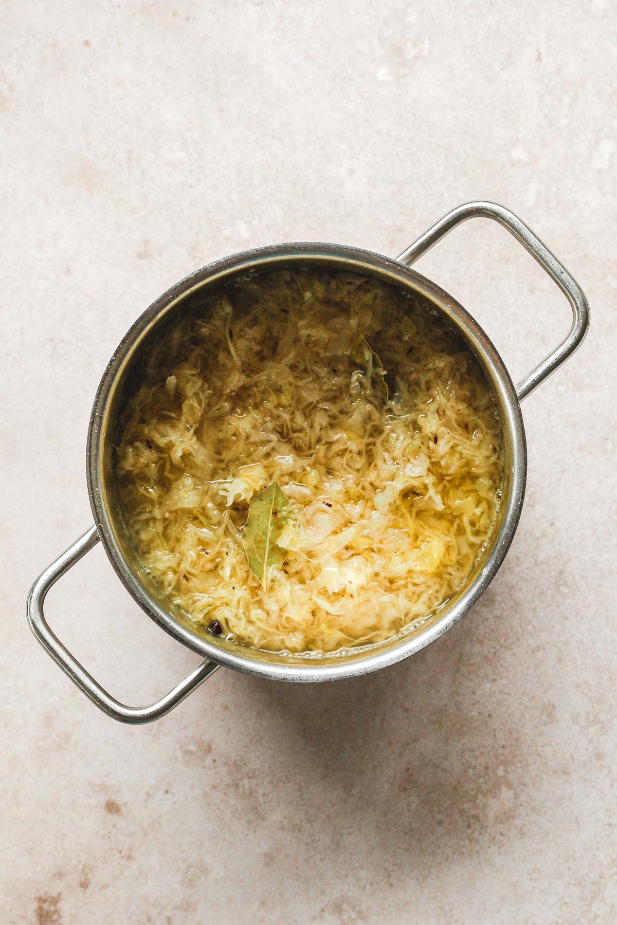 sauerkraut with spices and beef stock in pot on beige background.