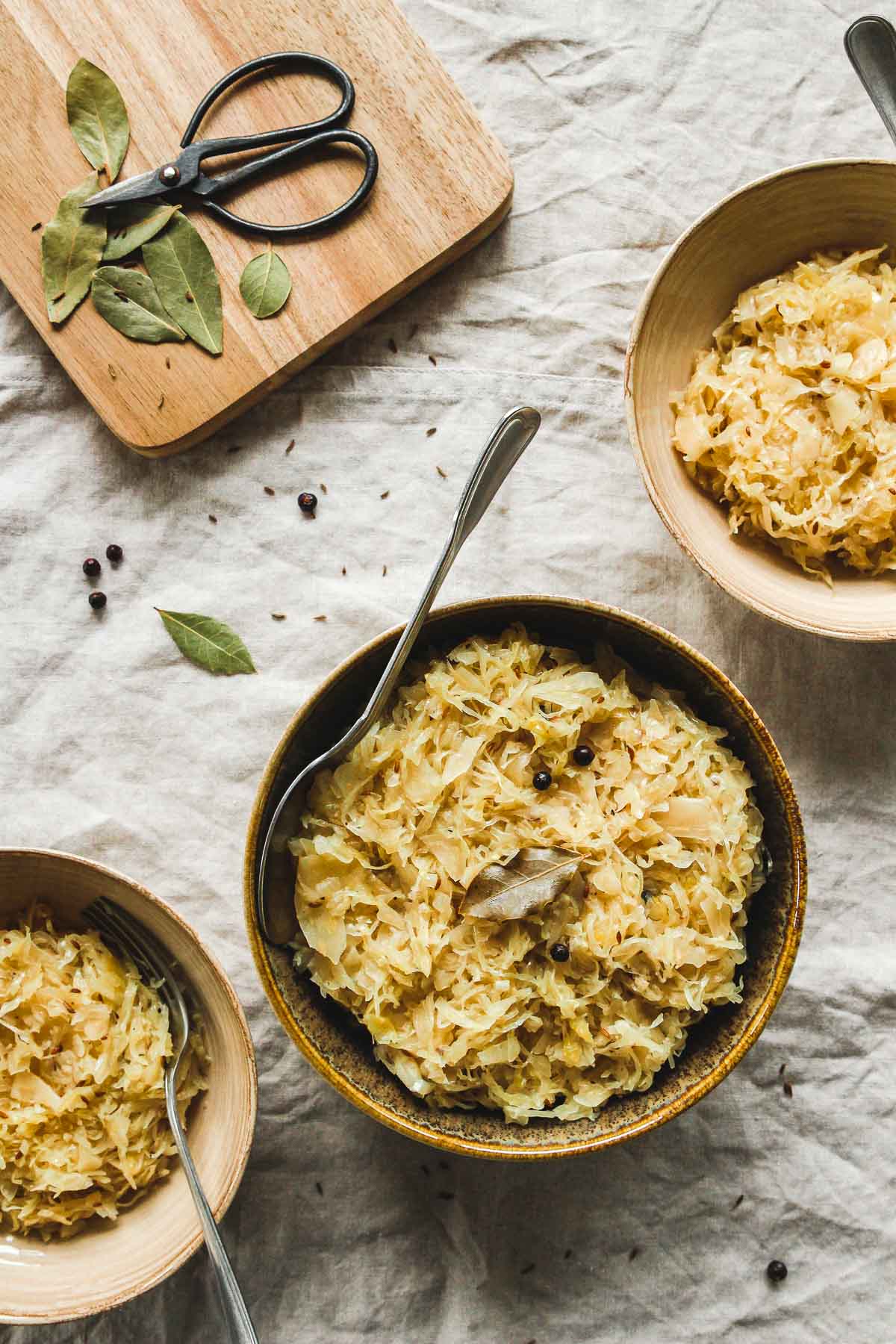 aromatic cooked sauerkraut in brown bowls with vintage spoon on beige tablecloth.