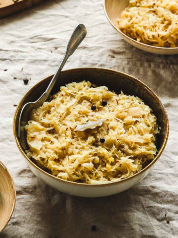aromatic cooked sauerkraut in brown bowls with vintage spoon on beige tablecloth.