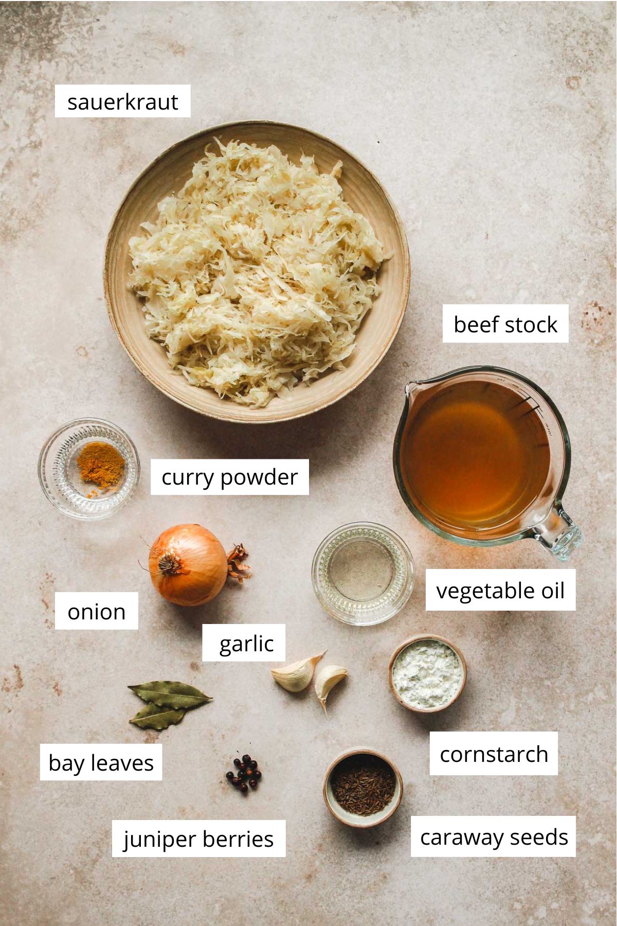 ingredients for cooked sauerkraut on rustic light brown background.