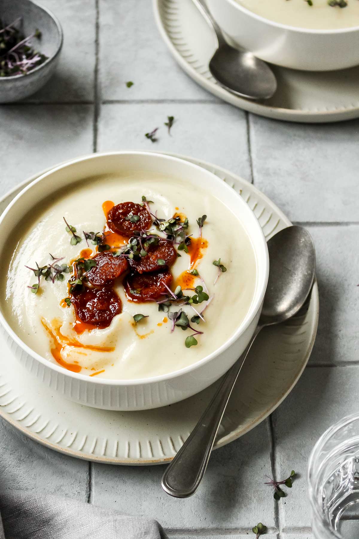 keto cauliflower soup in white bowl with vintage spoon on grey tile background.