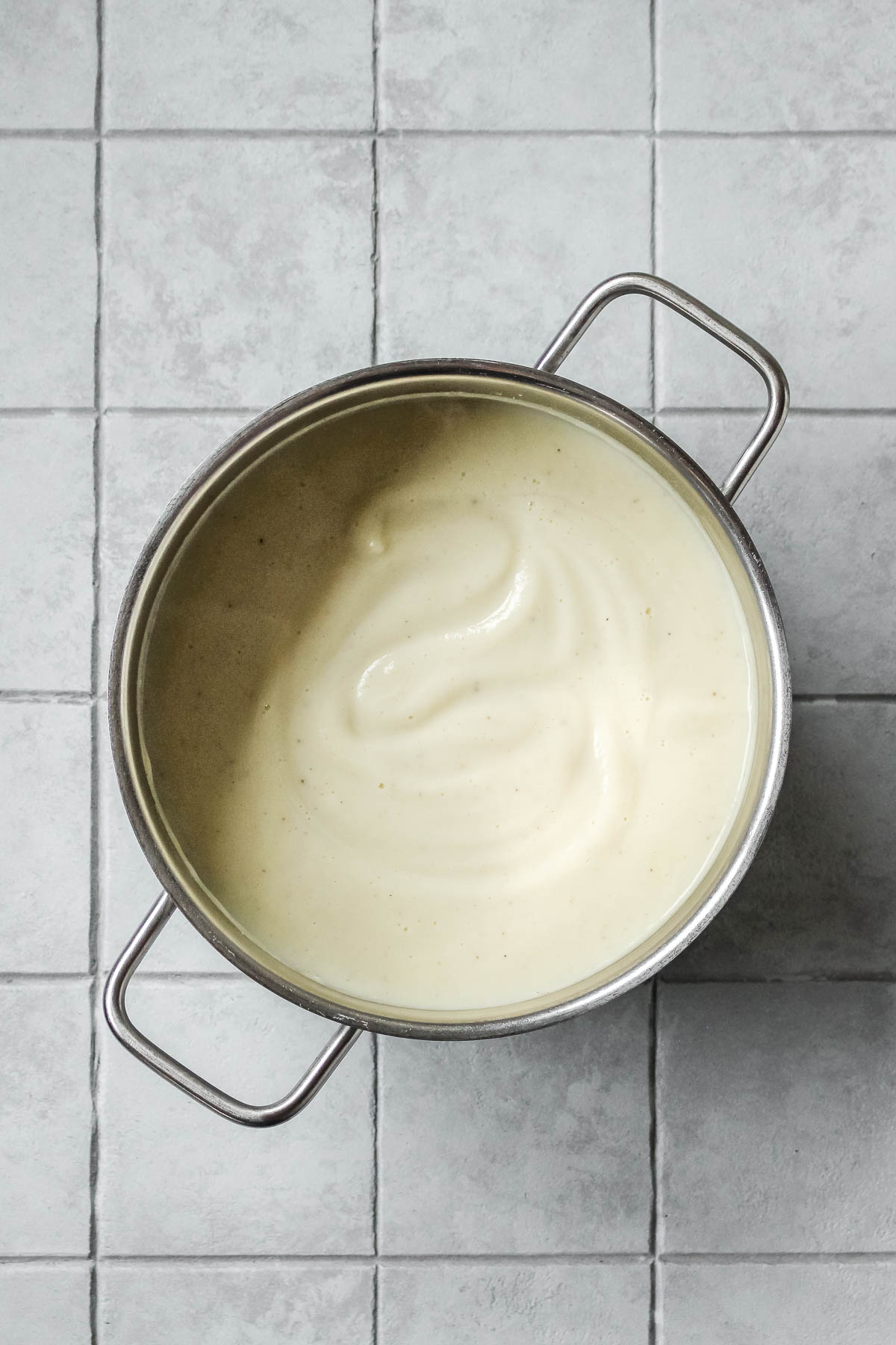 pureed cauliflower soup in pot on tile background.