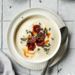 spicy cauliflower soup in white bowl with vintage spoon on grey tile background with props.