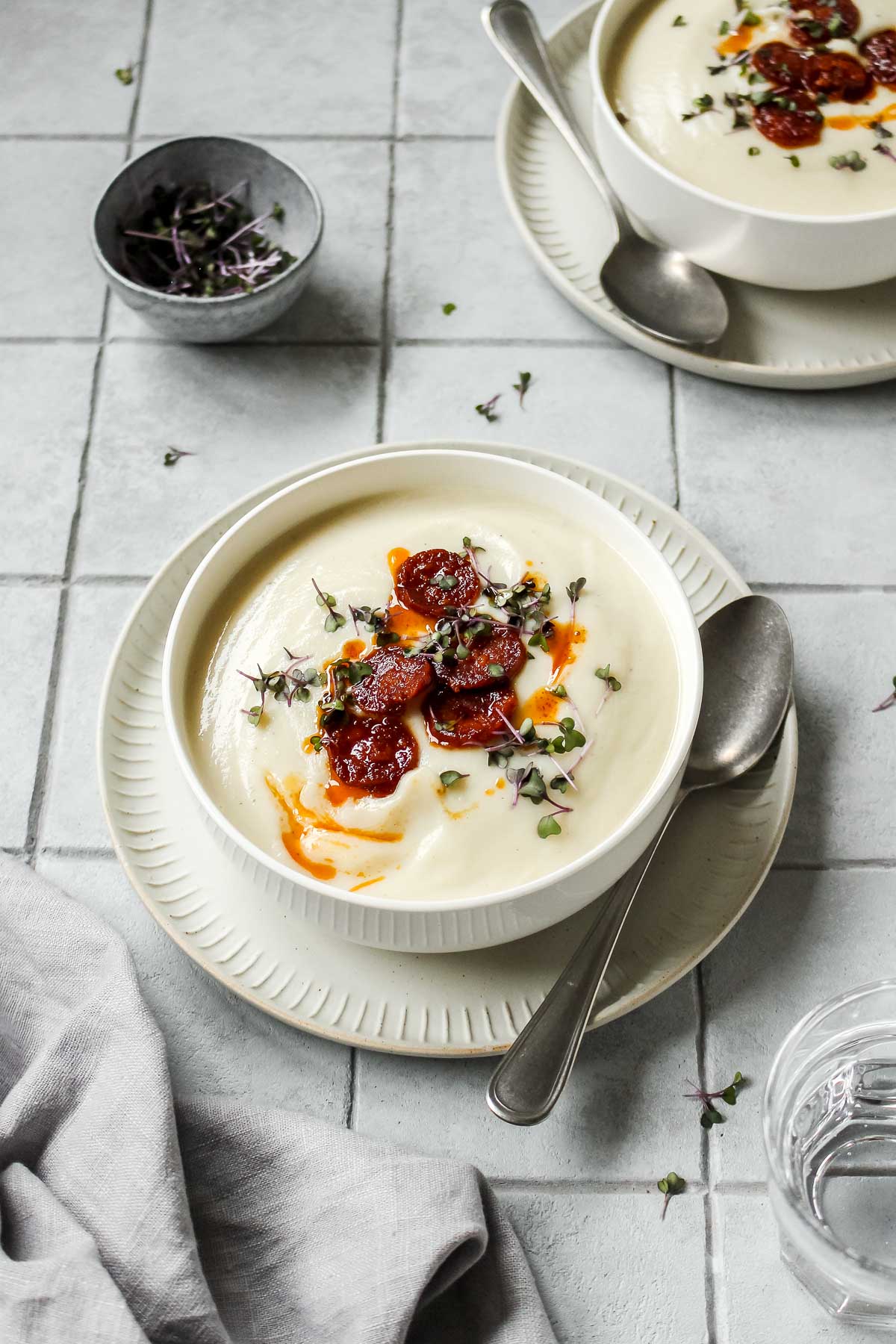 spicy cauliflower soup with chorizo and herb topping in white bowl with vintage spoon.