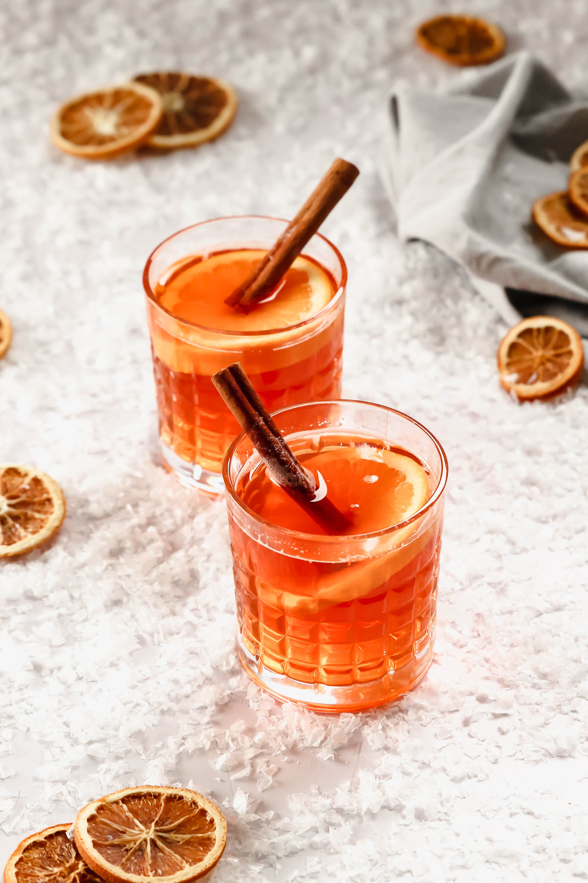 hot aperol in whisky glasses with orange and cinnamon garnish on background with snow.