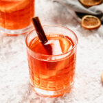 hot aperol in whisky glasses with orange and cinnamon garnish on background with snow.