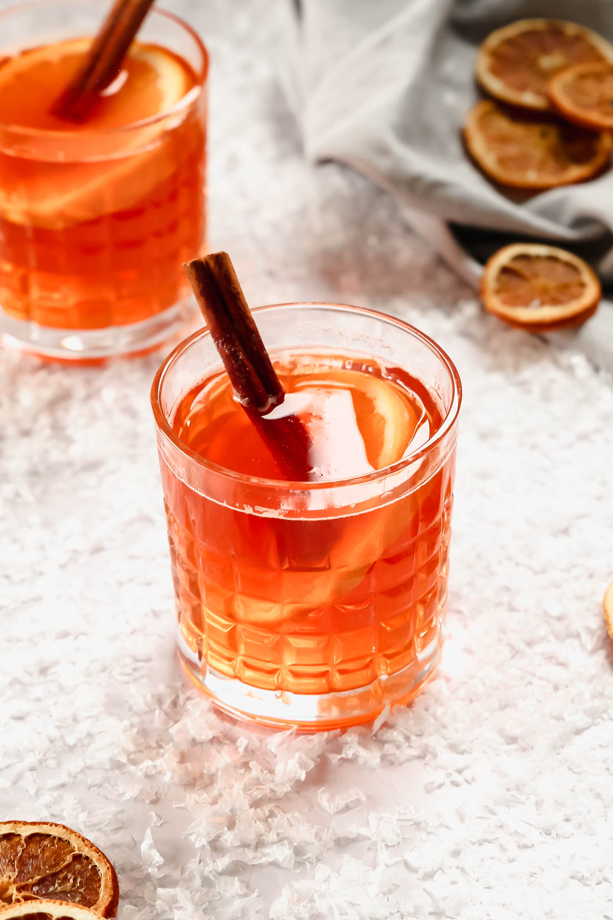 hot aperol in whisky glasses with orange and cinnamon garnish on background with snow.