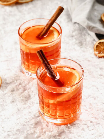 hot aperol in whisky glasses with orange and cinnamon garnish on background with snow.