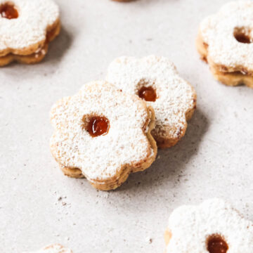 closeup of linzer cookies on grey background with confectioners sugar.