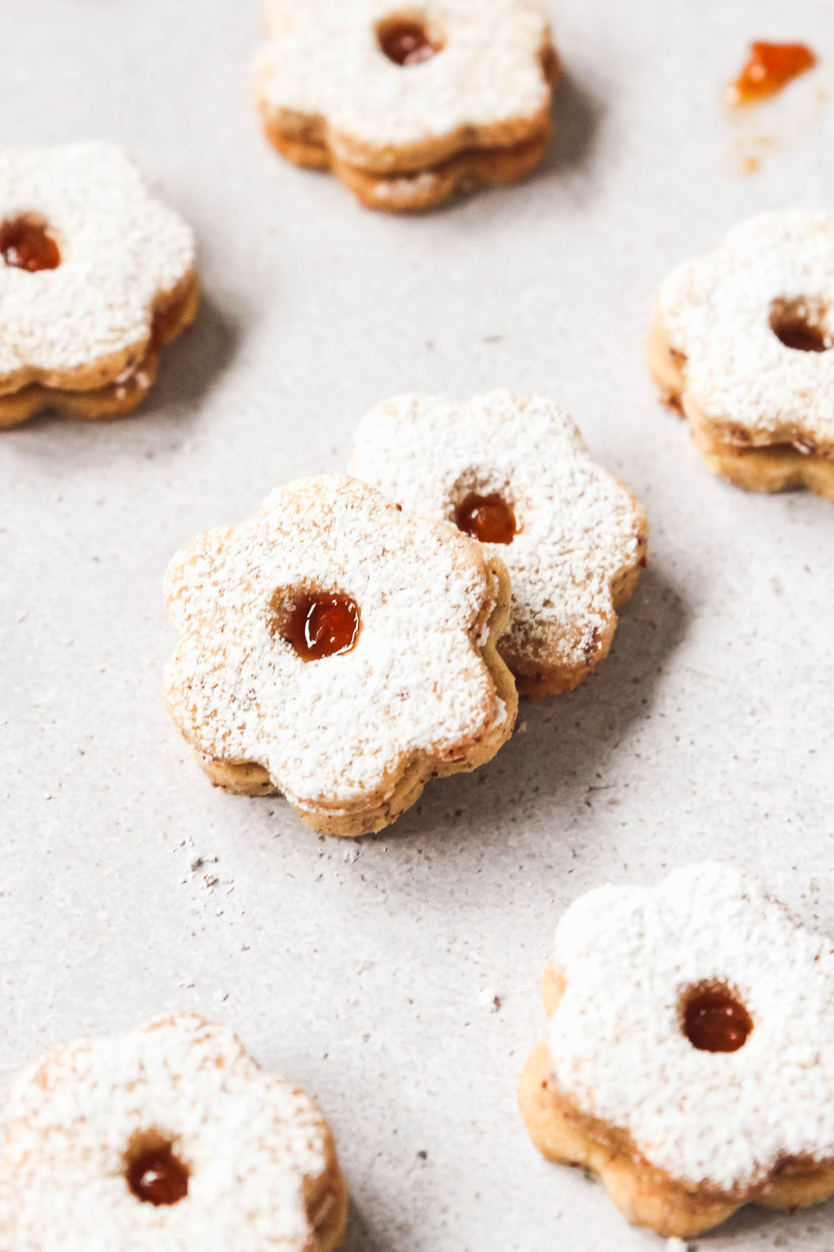 closeup of linzer cookies on grey background with confectioners sugar.