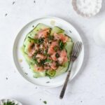 smoked salmon with herb vinaigrette and cucumber on white plate with vintage fork.