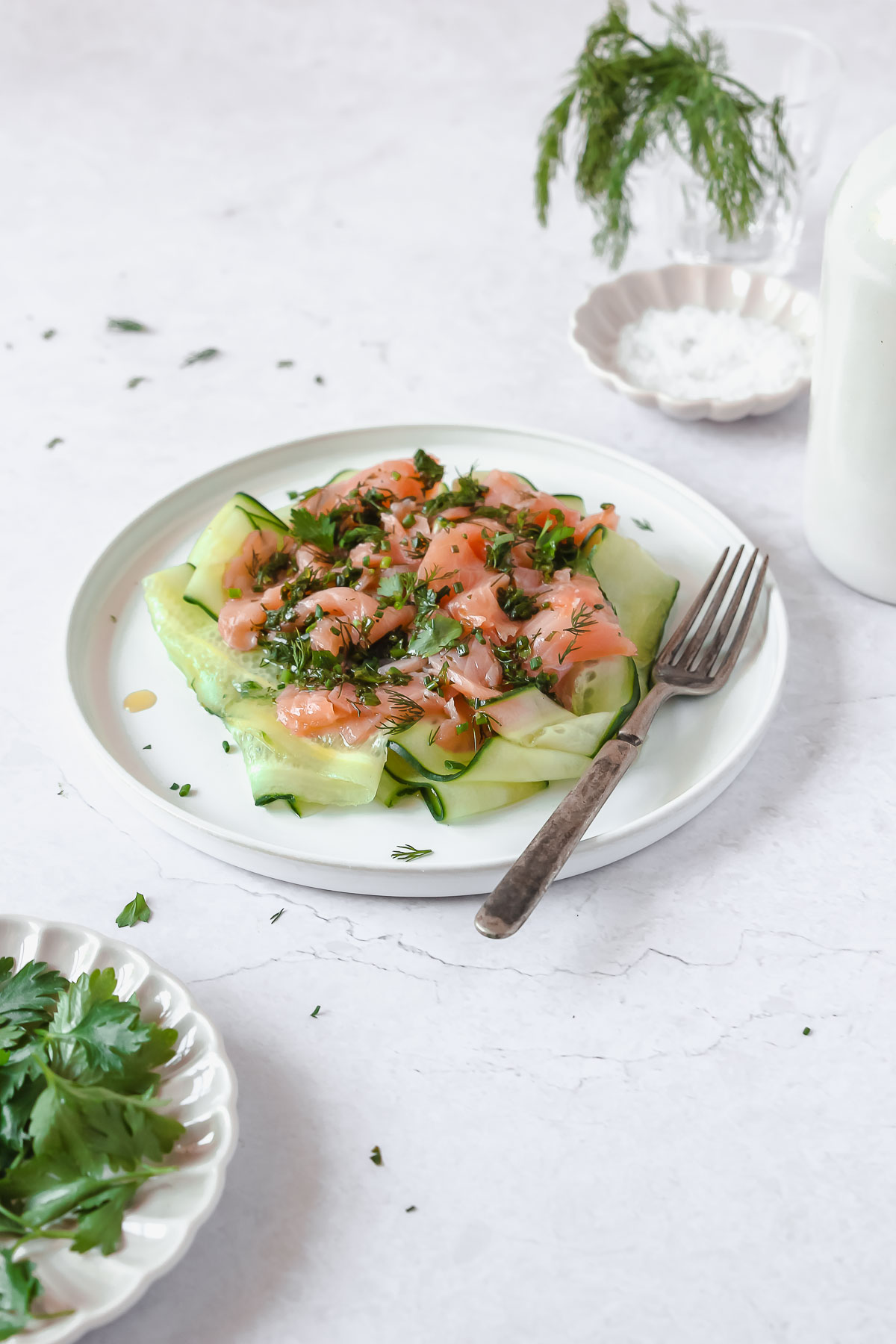 smoked salmon with herb vinaigrette and cucumber on white plate with vintage fork.